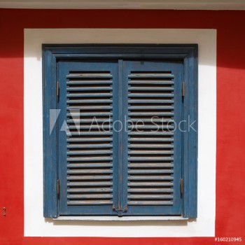 Picture of A beautiful old window on a red wall with closed blue shutters The window is photographed in the old town in Riga